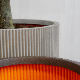 Close-up of two 3D-printed planters with ribbed texture, one planted with a tree Spoga+Gafa for Capi Europe