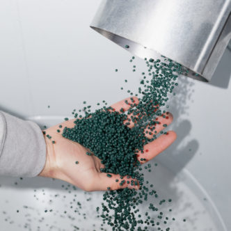 Hand catching green plastic granules pouring from a metal funnel